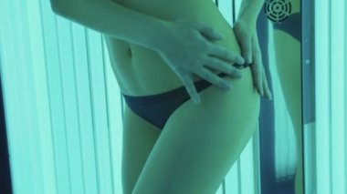 Bronzlaşma kabine ayakta ve vücut üzerinde bir krem uygulayarak çekici genç kadın.