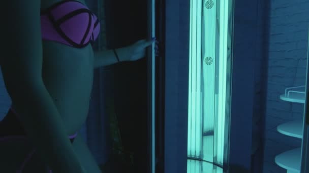 Mladá žena vstoupí do opalovací kabině v temné místnosti a zavře dveře. — Stock video