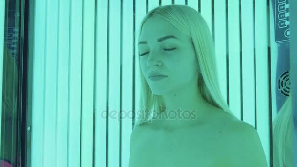 Attractive young blonde woman in pink swimsuit standing in tanning booth — Stock Video