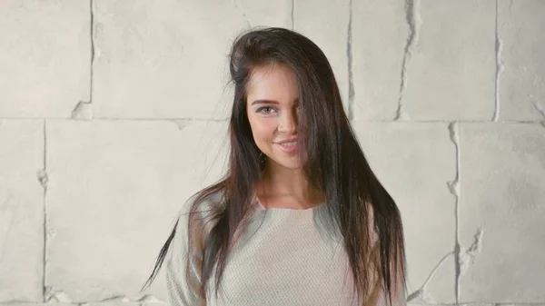 Ungdom-modellen i grå tröja tittar på kameran och leende över vit sten vägg. — Stockfoto