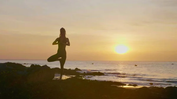 Практика йоги силуэта на закате. Yong woman doing yoga exercise on the beach — стоковое фото