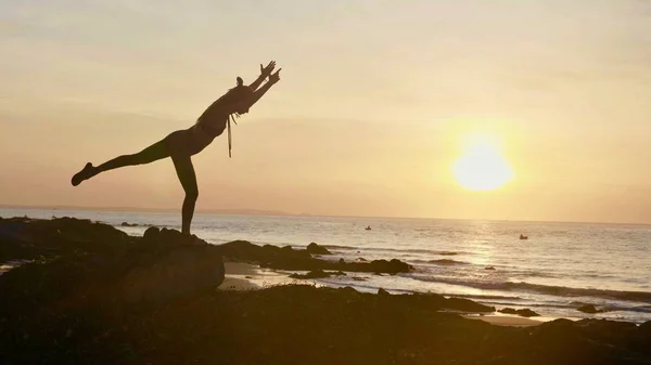 Практика йоги силуэта на закате. Yong woman doing yoga exercise on the beach — стоковое фото