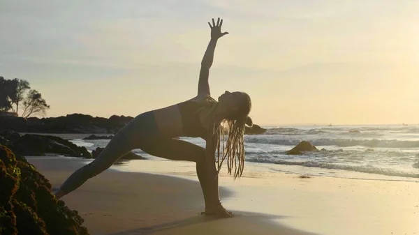 Практика йоги силуэта на закате. Yong woman doing yoga exercise on the beach — стоковое фото