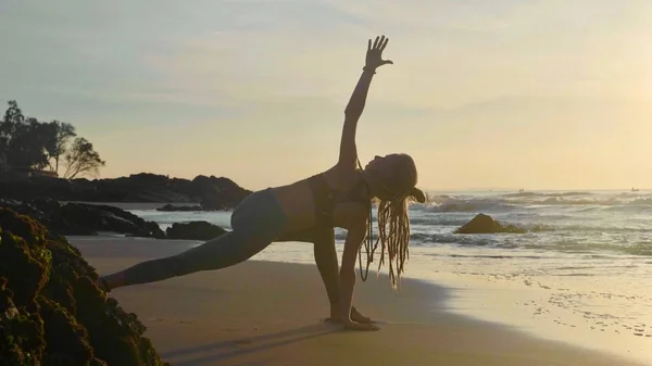 Практика йоги силуэта на закате. Yong woman doing yoga exercise on the beach — стоковое фото