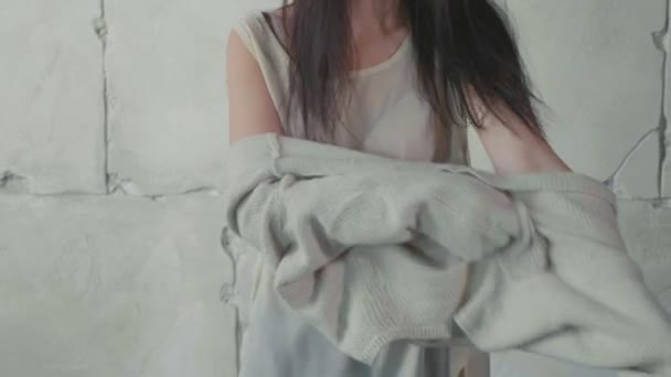 Молодежная модель одевает свитер над белой каменной стеной в замедленной съемке — стоковое видео