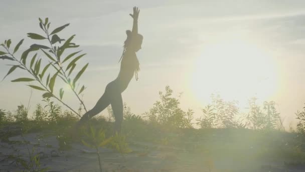 Silhueta de mulher fazendo exercícios de ioga em um parque ao nascer do sol em câmera lenta — Vídeo de Stock