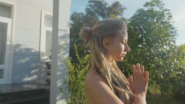 Молодая женщина, занимающаяся асаной йогой с жестами намаскар на заднем дворе своего дома — стоковое видео