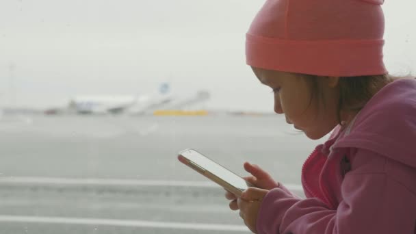 Schattig klein meisje met behulp van slimme telefoon in de luchthaven, close-up Slowmotion. — Stockvideo
