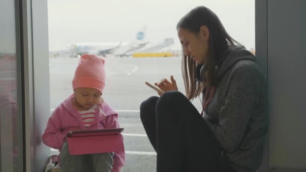Молодая мать и маленькая дочь используют устройства в аэропорту . — стоковое видео