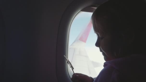 Silhueta criança menina chupando doces no madeira vara sobre porthole no avião — Vídeo de Stock