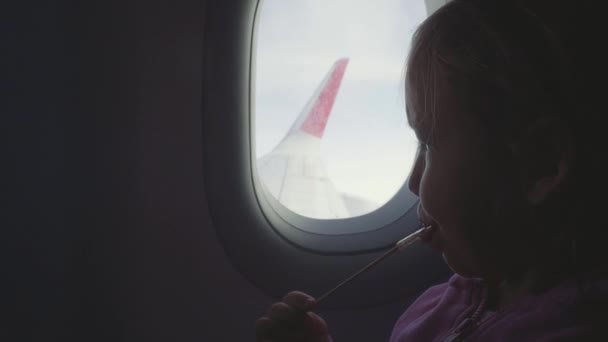 Силуэт ребенок девочка сосать сладости на деревянной палке над иллюминатором в самолете — стоковое видео