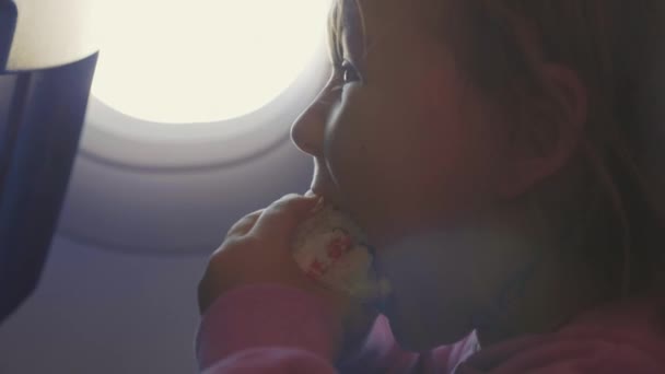 クローズ アップ子女の子が飛行機の舷窓を食欲でハンバーガーを食べる — ストック動画