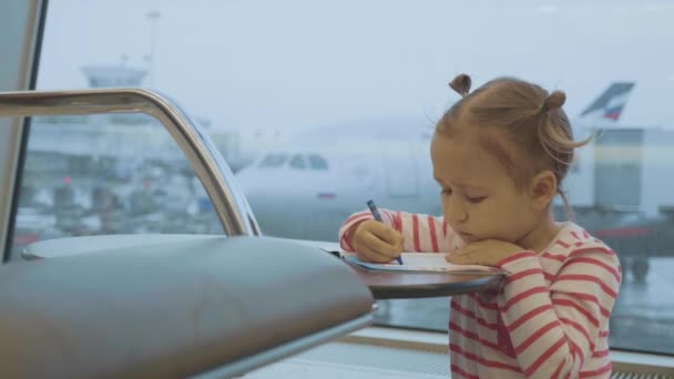 Piccola bambina che disegna all'aeroporto con aereo sullo sfondo — Video Stock