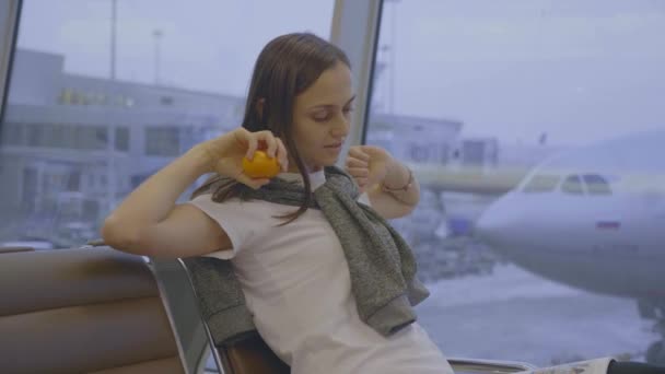 Mujer joven se sienta y se extiende en el aeropuerto con el avión en el fondo — Vídeo de stock