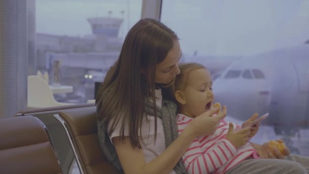 Madre alimenta a su pequeña hija con mandarina en el aeropuerto en cámara lenta — Vídeos de Stock