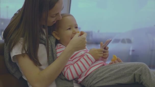 Moeder voedt haar dochtertje met tangerine op luchthaven in slow motion — Stockvideo