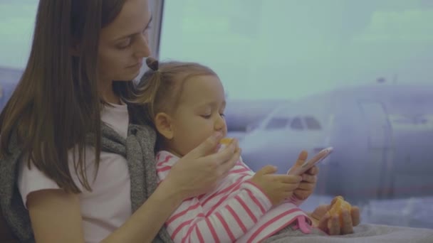 Mutter füttert kleine Tochter am Flughafen in Zeitlupe mit Mandarine — Stockvideo