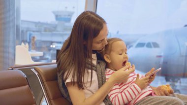 Anne küçük kızının havaalanında mandalina ile beslenir.