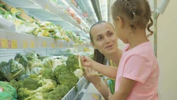 Ung mamma med lilla dotter att välja gröna grönsaker i livsmedelsbutik — Stockvideo