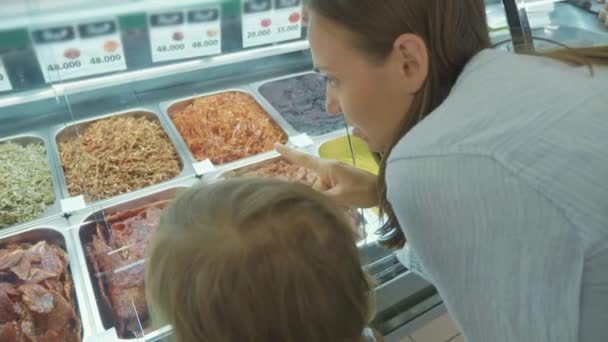 Madre joven con hija pequeña eligiendo comida preparada en el supermercado — Vídeo de stock