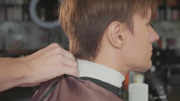 Nahaufnahme des Friseurs zieht dem männlichen Kunden den Umhang an, Zeitlupe. — Stockvideo