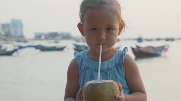 Malá holka pije kokosové vody u nábřeží na západ slunce v pomalém pohybu. — Stock video