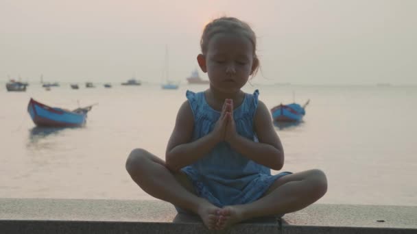 Aranyos kislány meditál török pózol a tengerparton — Stock videók