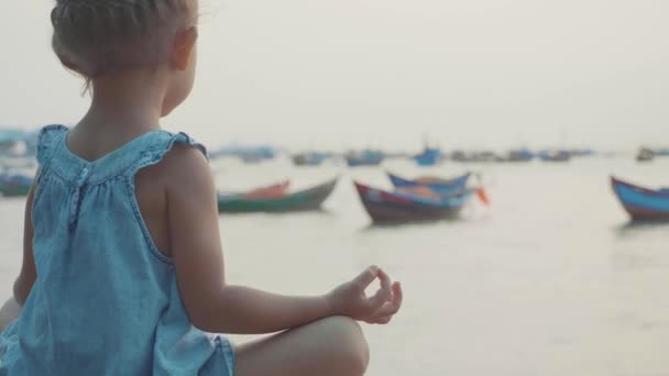 Kleines süßes Mädchen meditiert in türkischer Pose am Meer — Stockvideo