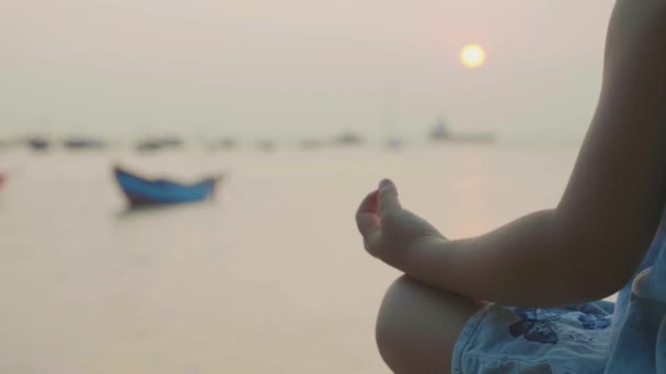 Kleines süßes Mädchen meditiert in türkischer Pose am Meer — Stockvideo