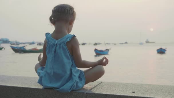 Niña linda medita en pose turca en primera línea de mar — Vídeos de Stock