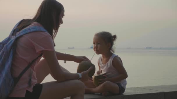 Podróżujący matka i córka siedzi nad brzegiem morza i napoje coconats w podróży — Wideo stockowe