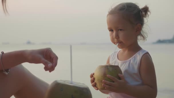 Travelers mother and daughter sits at seafront and drinks coconats in trip — Stock Video