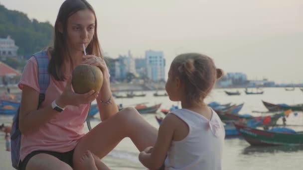 Travelers mother and daughter sits at seafront and drinks coconats in trip — Stock Video