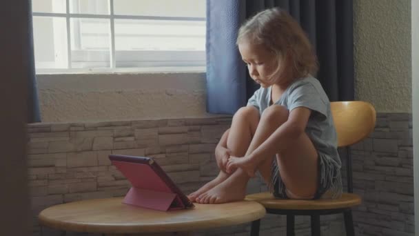 かわいい子女の子のテーブルに座って、タブレットで何かを見て — ストック動画