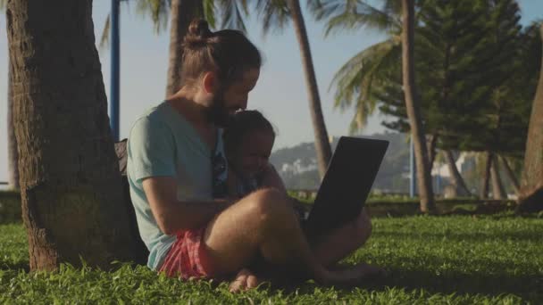 Hombre en el parque natural sentado con el ordenador portátil bajo una palmera . — Vídeos de Stock