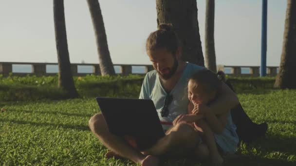 Otec s roztomilá holčička společně pomocí přenosného počítače v parku v pomalém pohybu. — Stock video