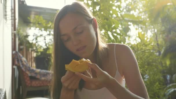 Портрет счастливой молодой женщины с удовольствием ест манго в зеленом саду — стоковое видео