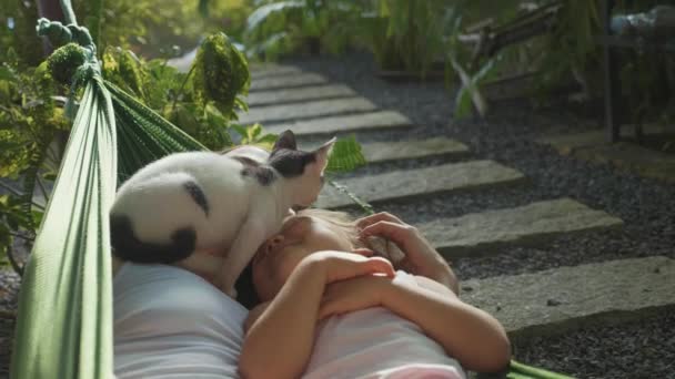 Onnellinen äiti ja tytär rentoutuvat yhdessä riippumatossa puutarhassa kesäpäivänä — kuvapankkivideo