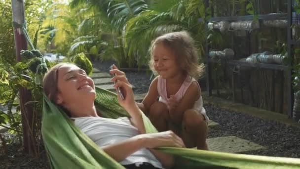 Woman tries uses a smartphone in a hammock and then plays with her daughter. — Stock Video