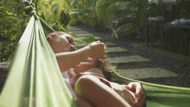 Mladá matka a dcera dohromady relaxaci v houpací síti na zahradě v letním dni — Stock video