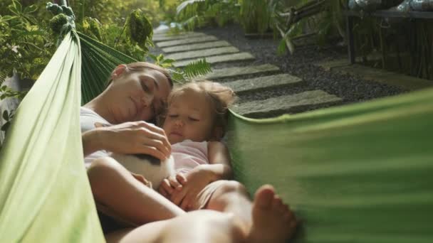 Ευτυχισμένη μητέρα και κόρη χαλαρωτικό μαζί σε μια αιώρα στον κήπο στη θερινή ημέρα — Αρχείο Βίντεο