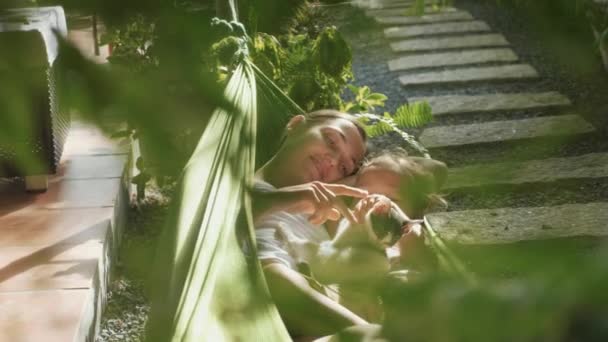 Feliz madre e hija relajándose juntas en una hamaca en el jardín en el día de verano — Vídeo de stock