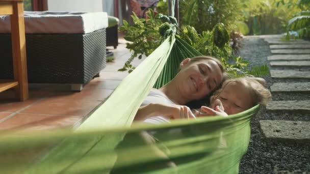 Feliz madre e hija relajándose juntas en una hamaca en el jardín en el día de verano — Vídeo de stock