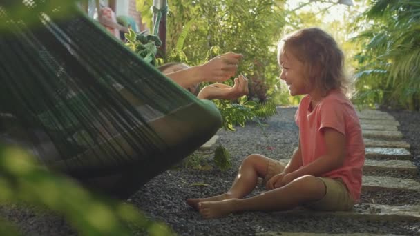 Jonge moeder liggend in een hangmat en spelen met haar dochtertje — Stockvideo