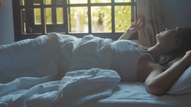 Porträtt av bara vaken ung kvinna ligger i sängen hemma på morgonen. — Stockvideo
