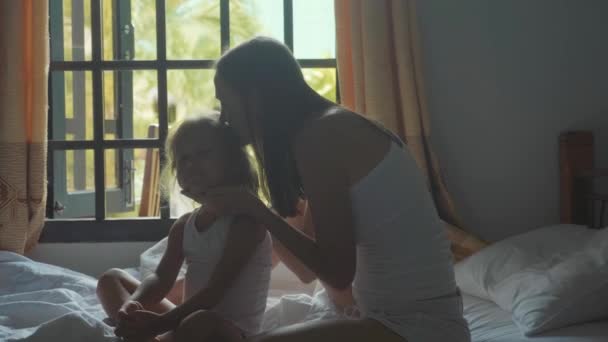 Jonge moeder zit op het bed en kammen van haar dochter in slow motion. — Stockvideo