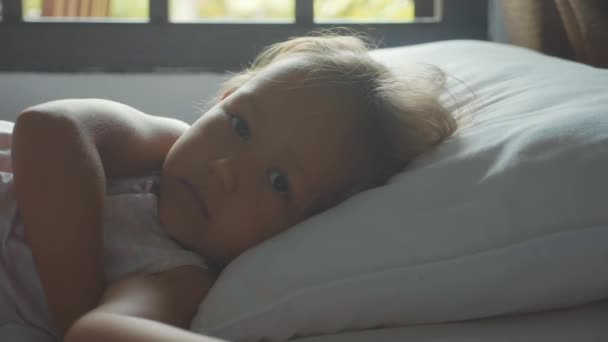 Portrait d'une enfant juste éveillée couchée au lit à la maison le matin . — Video