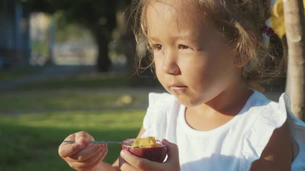 Primer plano de linda niña comiendo una fruta de la pasión al aire libre en cámara lenta — Vídeo de stock