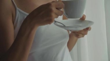 Genç kadın içecekler kahve evde, pencerenin yanında ağır çekimde yakın çekim