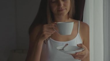 Genç kadın içecekler kahve evde, pencerenin yanında ağır çekimde yakın çekim